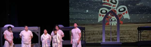 A picture of six indigenous actors on stage with dormitory bunks behind them and an image of a cathedral church window and an indigenous raven image beyond.